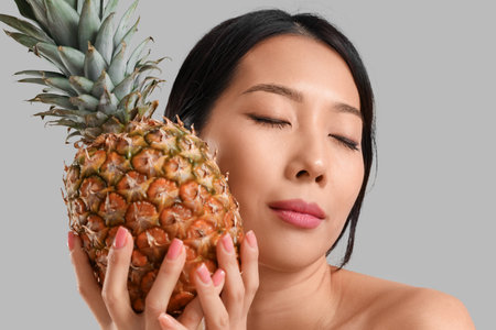 Pretty young Asian woman with pineapple on gray backgroundの写真素材