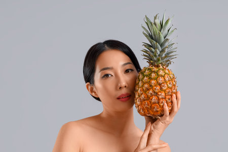 Pretty young Asian woman with pineapple on gray backgroundの写真素材