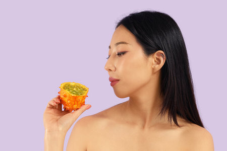 Pretty young Asian woman with kiwano on lilac backgroundの写真素材