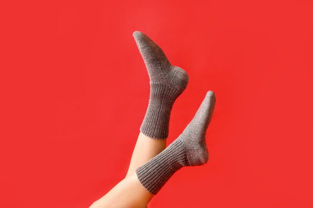 Legs of young woman in warm gray knitted socks on red backgroundの写真素材
