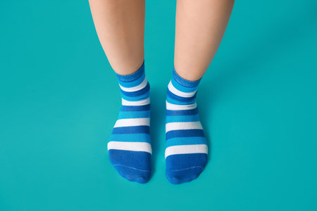 Legs of young woman in striped socks on blue background