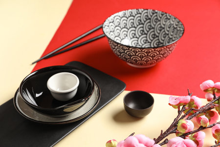 Bowls with cups, chopsticks and sakura branch on color background. Chinese table settingの写真素材
