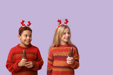 Cute little children in reindeer horns with chocolate Santa Claus on lilac backgroundの写真素材