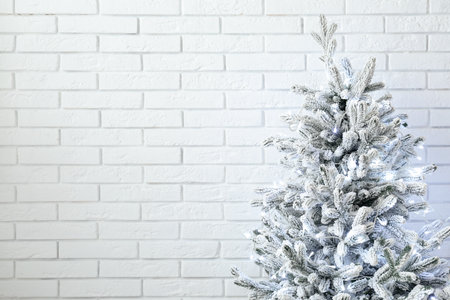Fir tree decorated for Christmas with garland near white brick wallの写真素材
