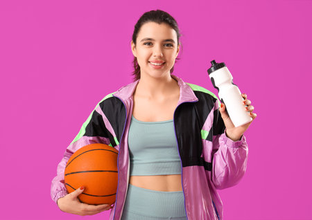 Young woman in sportswear with ball and water bottle on purple backgroundの写真素材