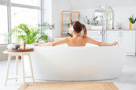 Beautiful woman with flower taking bath at home, back viewの写真素材