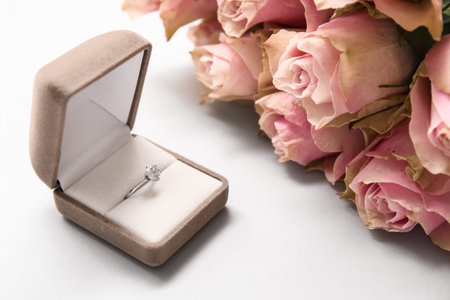 Box with beautiful engagement ring and pink roses on white background