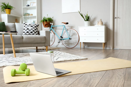 Laptop with dumbbells on fitness mat in living room