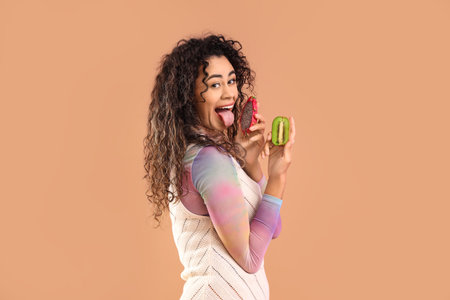 Young African-American woman with kiwi and dragon fruit on brown backgroundの写真素材