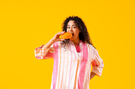 Young African-American woman eating pitahaya on yellow background