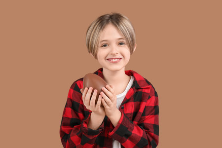 Happy little boy with chocolate egg on brown background. Easter celebration