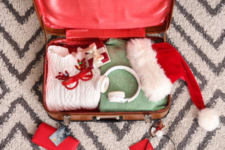 Suitcase with clothes, headphones, documents and Christmas decor on carpetの写真素材