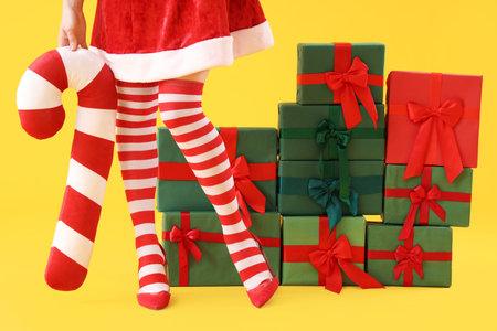 Sexy woman in Christmas stockings with cushion and stack of gifts on yellow backgroundの写真素材