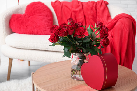 Bouquet of beautiful roses and gift box on table in room decorated for Valentine's Day celebrationの写真素材