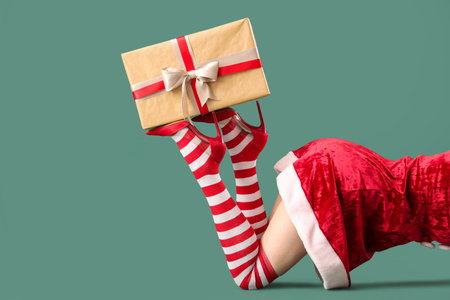 Sexy woman in Santa dress and Christmas stockings with gift box lying against green backgroundの写真素材