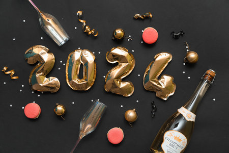 Figure 2024 made of foil balloons, champagne bottle with glasses and Christmas decor on black backgroundの写真素材