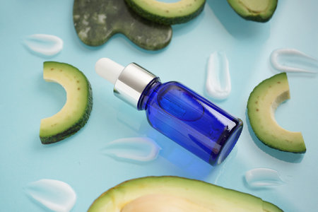 Composition with fresh cut avocado, cream samples and bottle of essential oil on blue background, closeupの写真素材