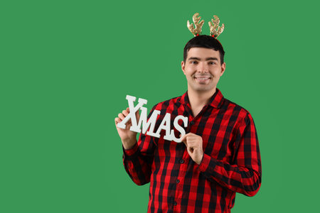 Young man in pajamas and deer horns with Christmas decor on green backgroundの写真素材