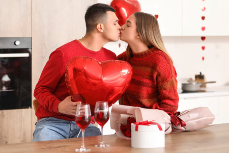 Beautiful young couple with heart-shaped balloon, gift box and wine glasses celebrating Valentine's...