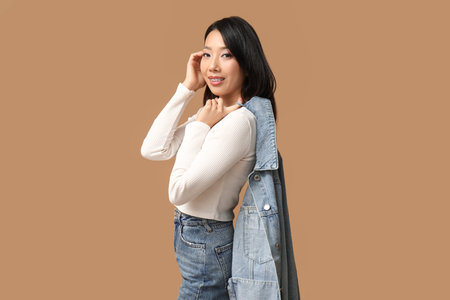 Beautiful young happy Asian woman in stylish denim clothes on brown background