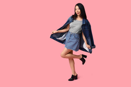 Beautiful young happy Asian woman in stylish denim clothes on pink backgroundの写真素材