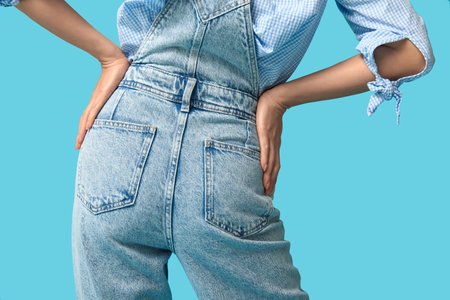 Beautiful young Asian woman in stylish denim jumpsuit on blue background, back viewの写真素材