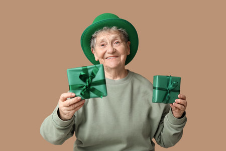 Senior woman in leprechaun hat with gift boxes on brown background. St. Patrick's Day celebrationの写真素材