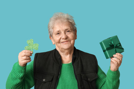 Senior woman with clover and gift box on blue background. St. Patrick's Day celebrationの写真素材