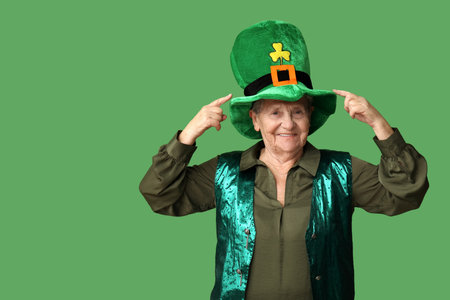 Senior woman pointing at leprechaun hat on green background. St. Patrick's Day celebrationの写真素材