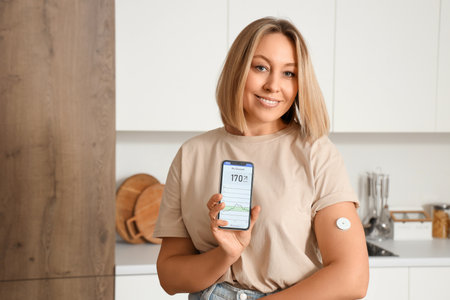 Diabetic woman with glucose sensor using mobile phone for measuring blood sugar level in kitchenの写真素材
