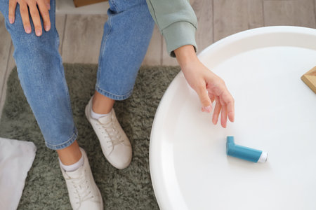 Young woman taking asthma inhaler from table at home, closeupの写真素材