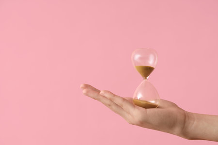 Female hand holding hourglass on pink backgroundの写真素材
