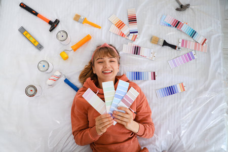 Young woman with color palettes and paint tools lying on bed, top viewの写真素材