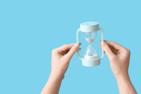 Female hands holding hourglass on blue backgroundの写真素材