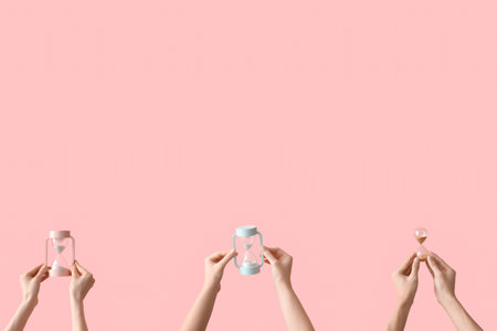 Female hands holding hourglasses on pink background