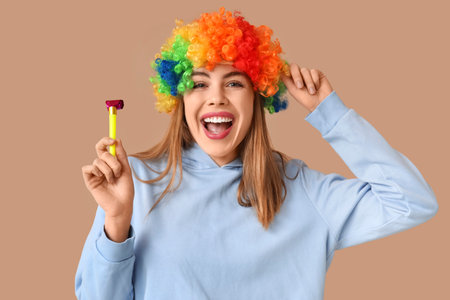 Beautiful young happy woman in funny disguise with party whistle on brown background. April Fools Day celebrationの写真素材