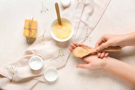 Female hands with body scrub and cosmetic products on light backgroundの写真素材