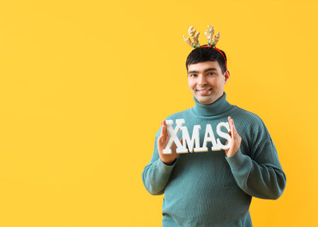 Young man in deer horns with Christmas decor on yellow backgroundの写真素材