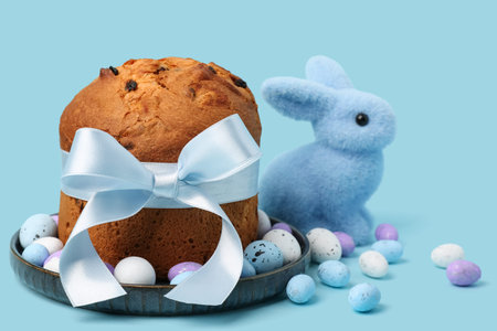 Plate with delicious Easter cake, painted eggs and bunny on blue background