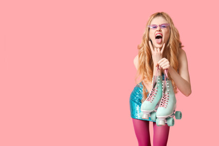 Beautiful young happy woman with vintage roller skates showing devil horns gesture on pink...