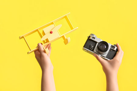 Female hands with toy plane and vintage photo camera on yellow background, closeupの写真素材