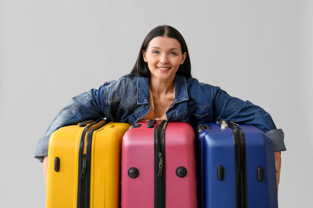 Beautiful young woman with different suitcases on gray backgroundの写真素材