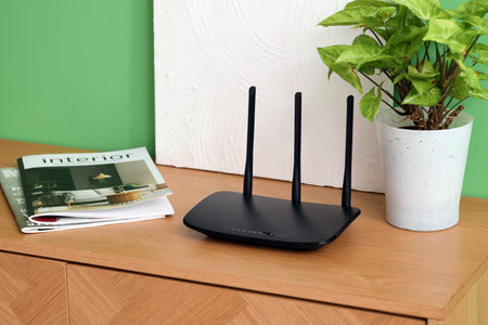 Modern wi-fi router with plant, magazines and painting on commode near green wallの写真素材