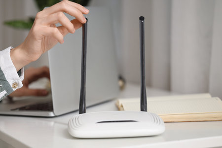 Modern wi-fi router on table of working woman with laptop, closeup