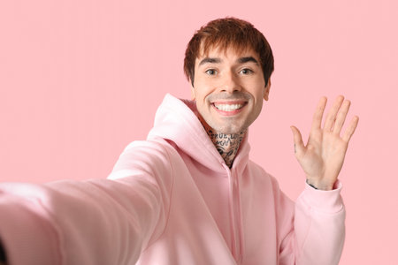 Happy handsome young tattooed man waving hand on pink backgroundの写真素材
