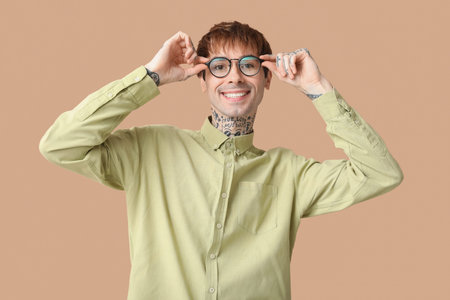Happy handsome young tattooed man in eyeglasses on beige background