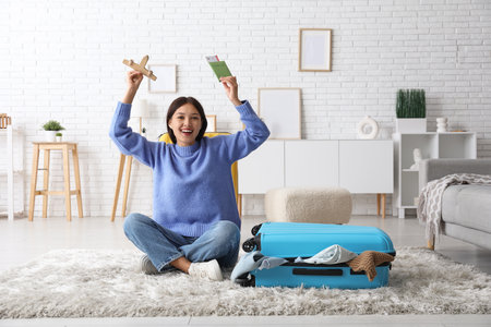 Young woman with wooden plane, passport and suitcase sitting on floor at homeの写真素材