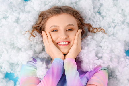Young woman lying on white cloud against blue background, top viewの写真素材