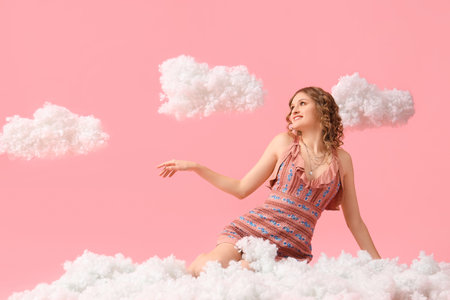 Young woman with white clouds sitting on pink backgroundの写真素材