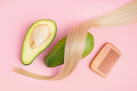 Fresh avocado, hair strand and comb on pink background